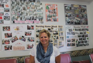 Activities Director Trish St Amand in front of posters documenting and  celebrating the events that have taken place at the Manor 